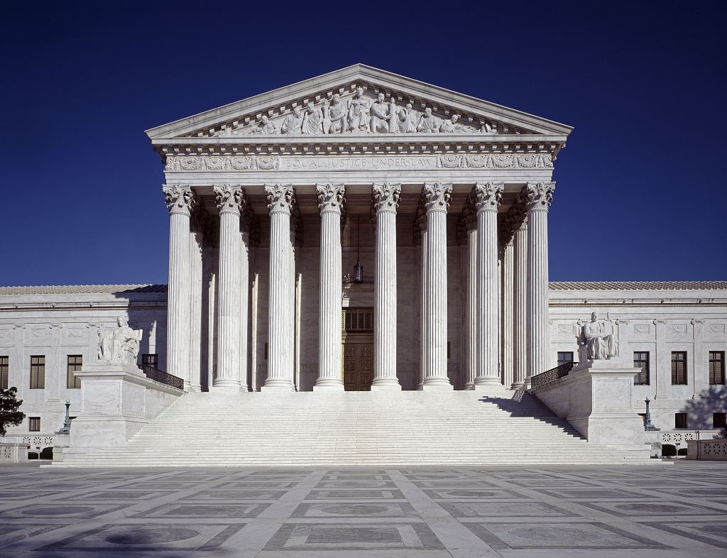 Front exterior of the United States Supreme Court Building in Washington, D.C., beneath a deep blue sky.